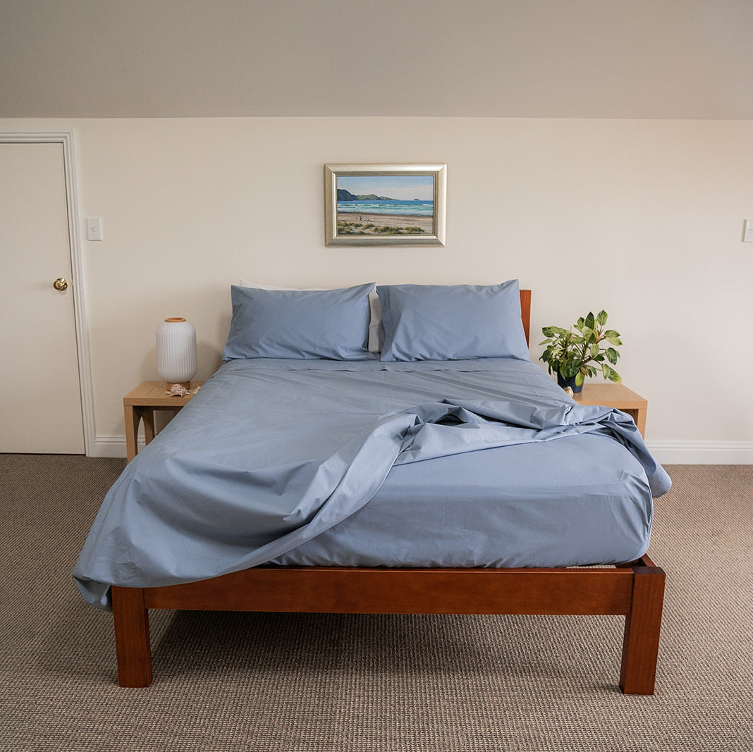 Bed  with blue cotton bedding, showing fitted sheet detail, set in bedroom with 2 side tables and seaside picture on wall