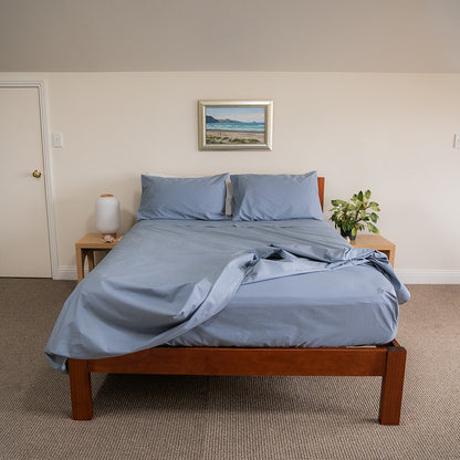Bed  with blue cotton bedding, showing fitted sheet detail, set in bedroom with 2 side tables and seaside picture on wall