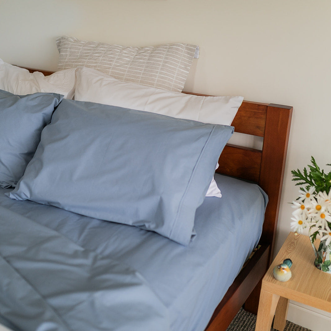 Bed with blue linen highlighting fitted sheet and pillowcase, side table has flowers in vase and bird ornament 