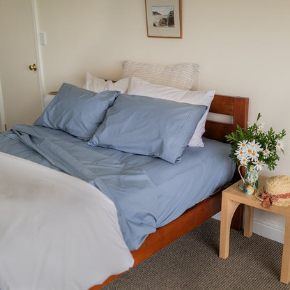 bed with blue cotton sheets & pillows and side table featuring white flowers 