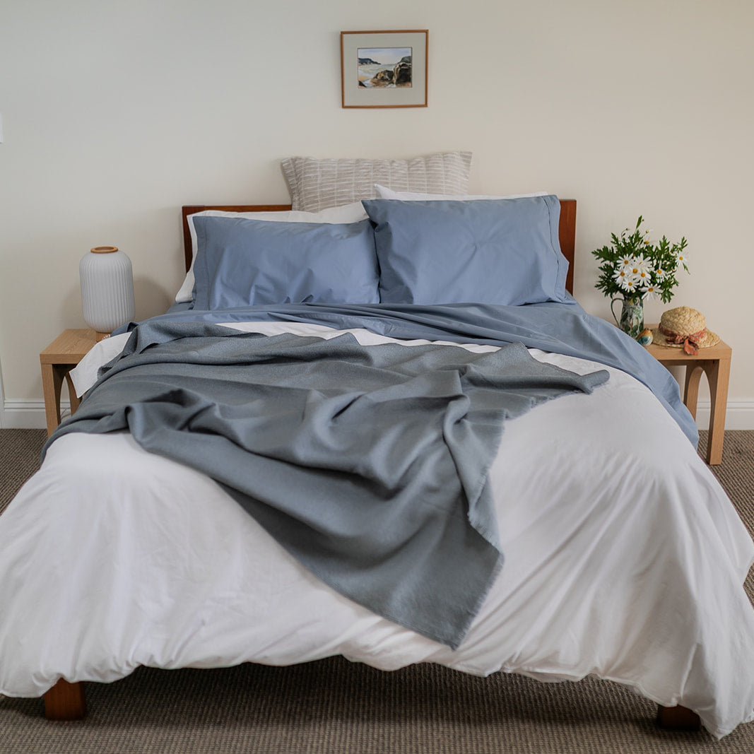 Bedroom with a bed featuring blue bedding , gray throw blanket, nightstands with lamps, and a vase of flowers.