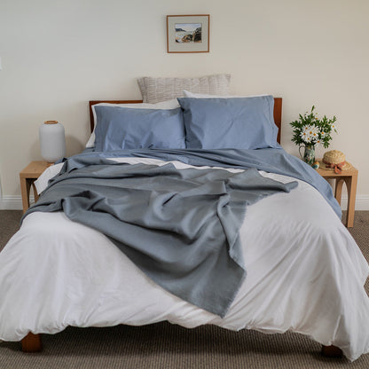 Bedroom with a bed featuring blue bedding , gray throw blanket, nightstands with lamps, and a vase of flowers.