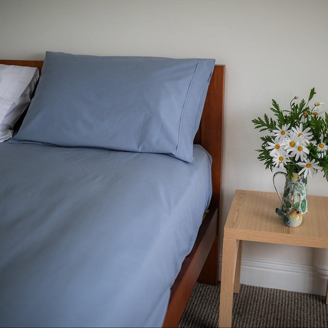 SleepFROG blue fitted sheet and pillowcase on bed with vase of white flowers on bedside table 
