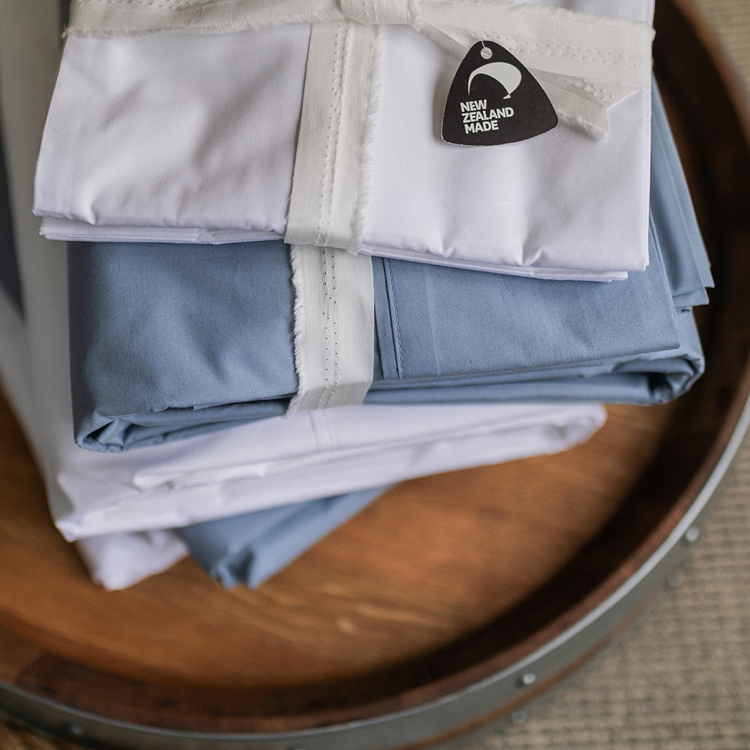Stack of SleepFROG blue and white flat sheets on a barrel top with made in NZ tag 