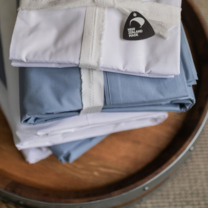 Stack of SleepFROG blue and white flat sheets on a barrel top with made in NZ tag 