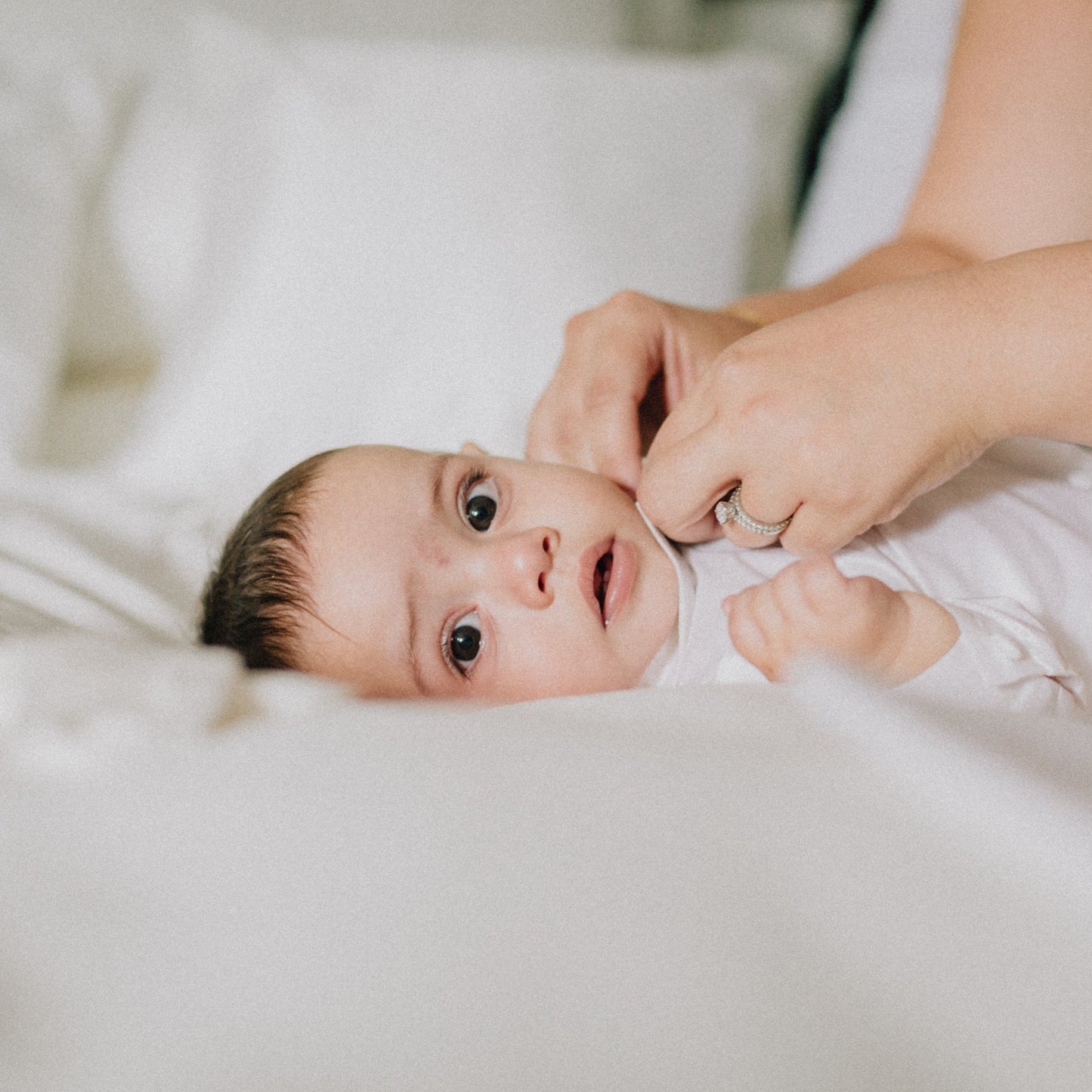 Baby lying on a white sheet  as Mum dresses them