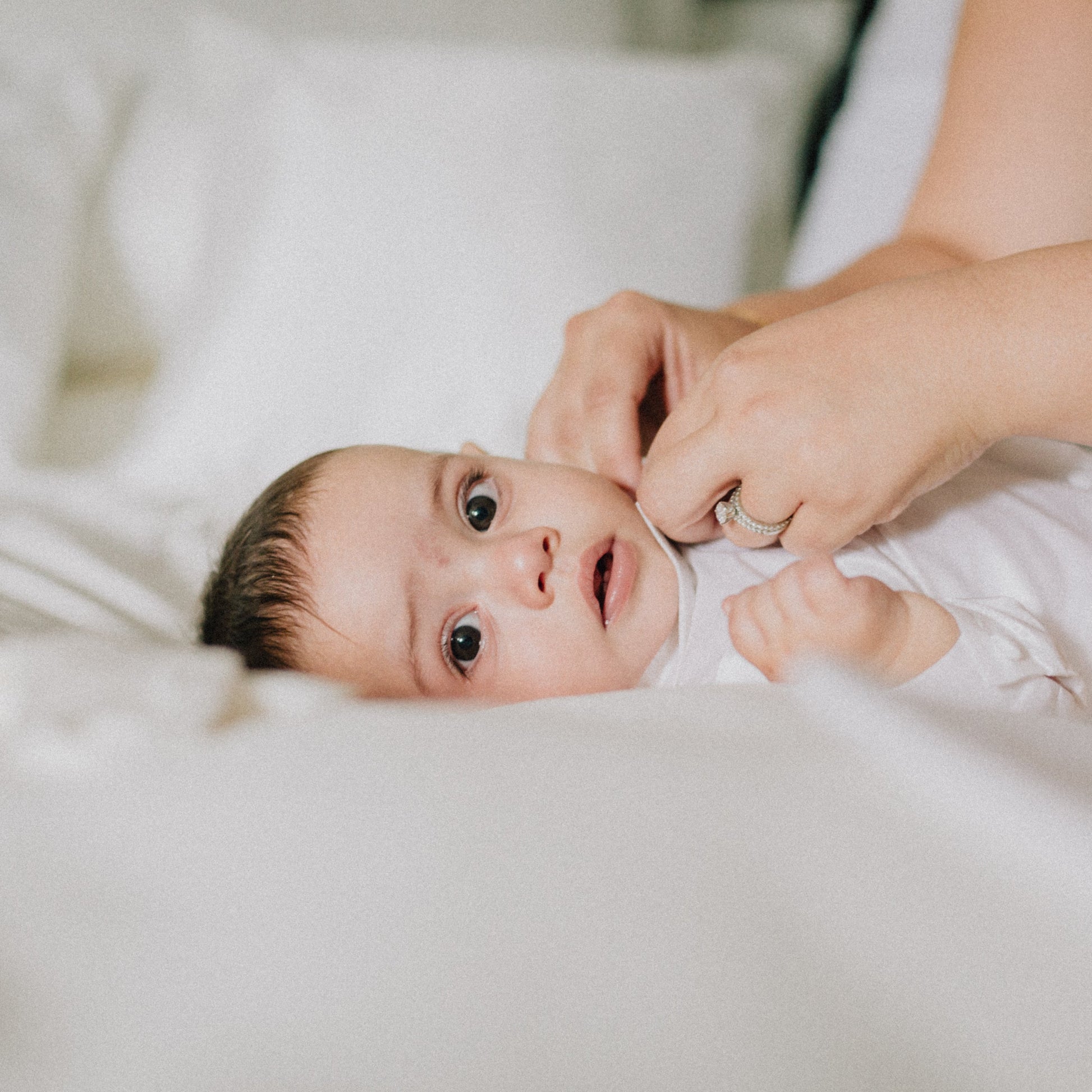 Baby lying on a white sheet  as Mum dresses them