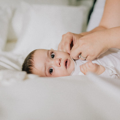 Baby lying on a white sheet  as Mum dresses them